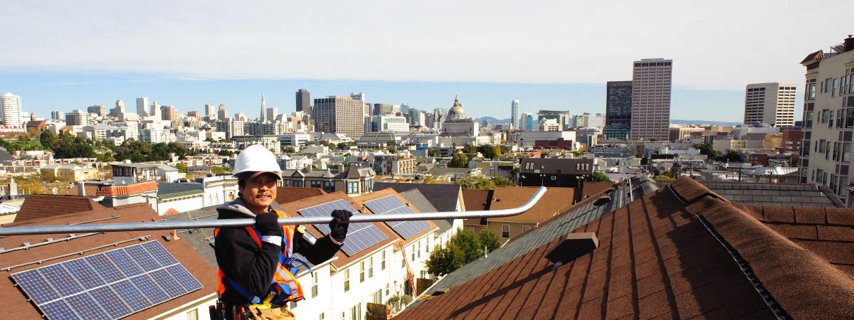 A man works on the roof of apartment buildings in San Francisco installing solar panels