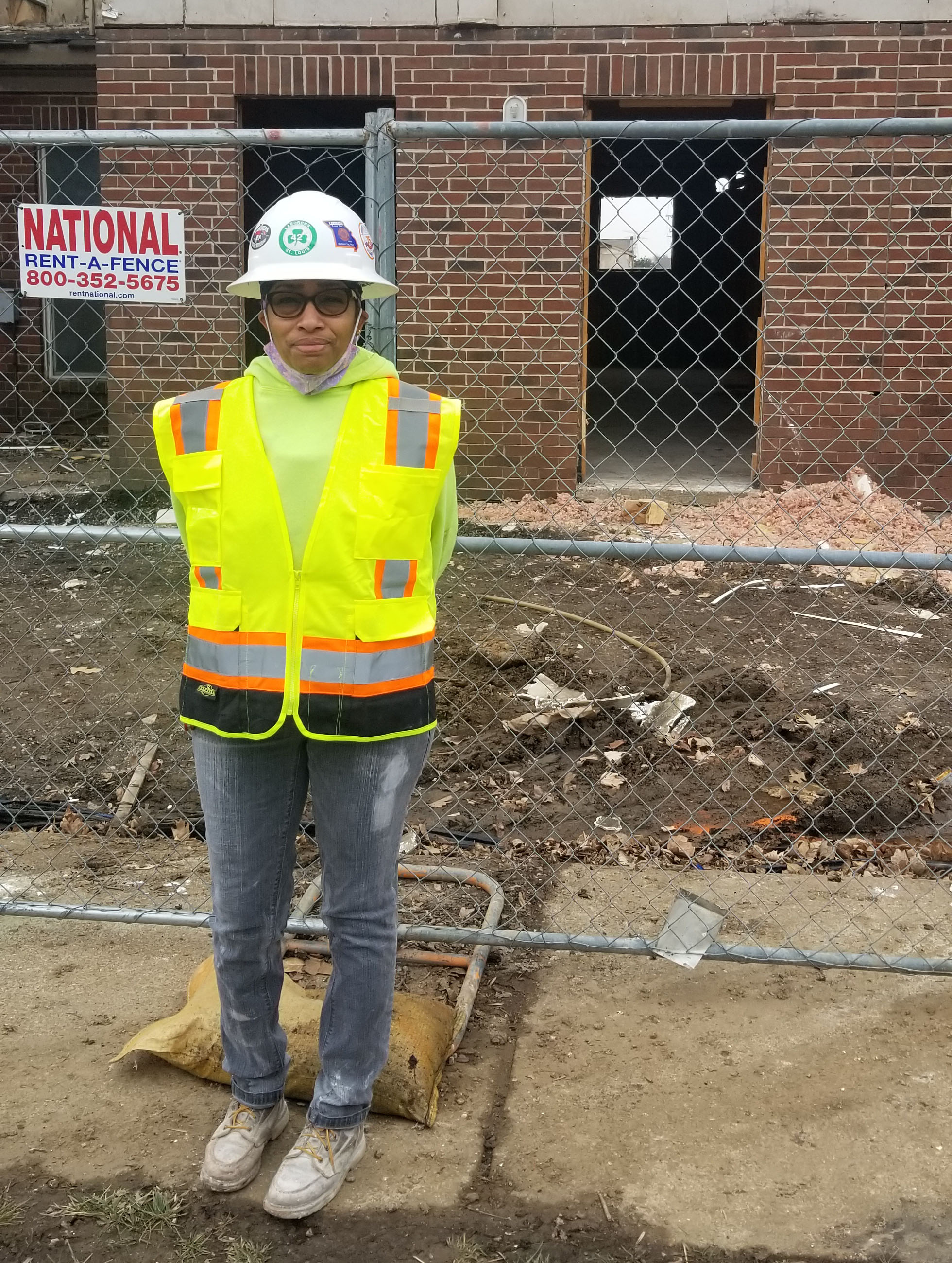 Della Tolliver in a safety vest in front of a brick building being renovated.